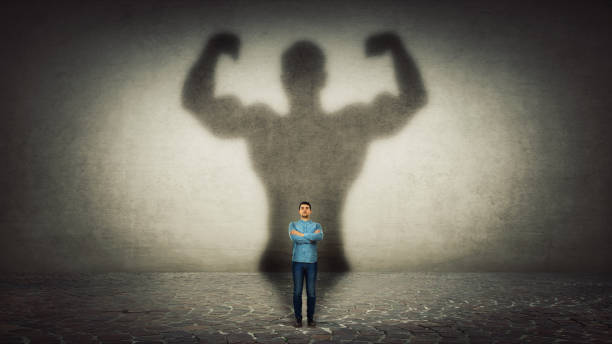 Confident businessman imagine himself a powerful hero, casting shadow of big strong muscular bodybuilder showing his biceps. Inner strength, leadership qualities. Business development.